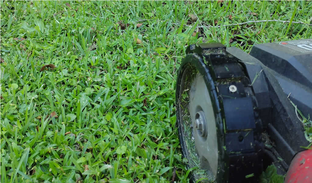 A close-up photo of the lower part of a lawn mower. The image focuses on the green tread of a deep-treaded lawn mower wheel Attachment. The tread pattern is designed for improved traction on difficult terrain.